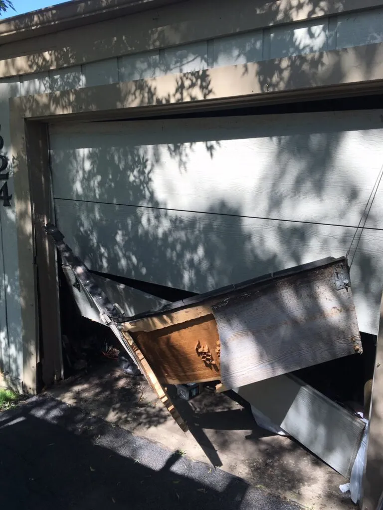 Impact-damaged garage door section with broken hardware needing repair inspection